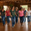 Women line dancing in More Than Just Steps V-neck graphic shirts inside a rustic barn